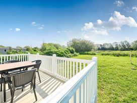 An outdoor deck with a table and chairs overlooking a grassy field with trees and a blue sky at Tranquil Waters - Billing Aquadrome in Billing Aquadrome Holiday Park