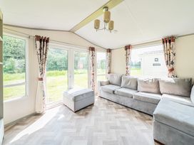 A living room with a gray sectional sofa and ottoman next to large windows with patterned curtains at Tranquil Waters - Billing Aquadrome in Billing Aquadrome Holiday Park