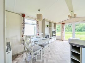 A dining area with a table set for four near large windows and a shelving unit with a television at Tranquil Waters - Billing Aquadrome in Billing Aquadrome Holiday Park