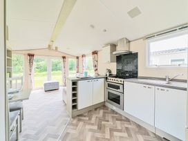 A kitchen and dining area with white cabinets a stove and large windows with curtains at Tranquil Waters - Billing Aquadrome in Billing Aquadrome Holiday Park