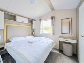 A bedroom with a bed a window with curtains and a dressing table with a mirror at Tranquil Waters - Billing Aquadrome in Billing Aquadrome Holiday Park