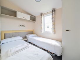 A bedroom with two single beds a window with curtains and overhead storage at Tranquil Waters - Billing Aquadrome