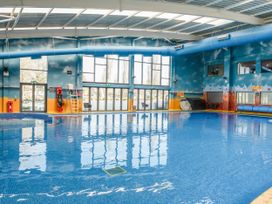 An indoor swimming pool with blue water and large windows in a blue and orange room at Aquadrome Abode - Billing Aquadrome Holiday Park