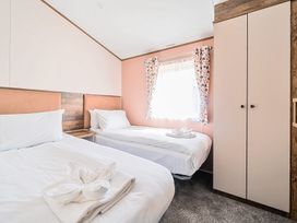 A bedroom with two single beds a window with patterned curtains and a wardrobe at Aquadrome Abode - Billing Aquadrome Holiday Park