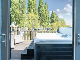 A deck with a hot tub and two wicker chairs overlooking a grassy area with trees at Aquadrome Abode - Billing Aquadrome Holiday Park