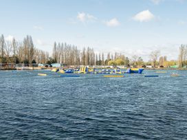 A lake with an inflatable water park and trees and buildings in the background at Moonlit Skylight - Billing Aquadrome in Billing Aquadrome Holiday Park