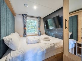 A bedroom with a bed white linens a window with curtains a wall mounted TV and a wardrobe with mirrored door at Moonlit Skylight - Billing Aquadrome in Billing Aquadrome Holiday Park