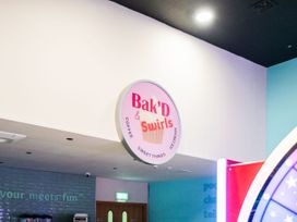 A round Bak'D and Swirls sign above a cafe entrance with blue brick wall and double wooden doors at Willowbrook Hideaway - Billing Aquadrome Holiday Park