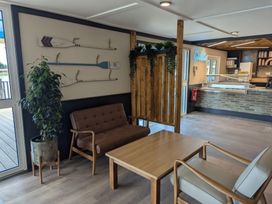 A seating area with a brown couch, a beige chair, a wooden table, a potted plant, and decorative oars on the wall near a gelato counter at Willowbrook Hideaway - Billing Aquadrome Holiday Park