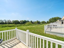 View of multiple outdoor decks with white railings facing a grassy area and trees at Island Breeze - Hayling Island in Hayling Island Holiday Park