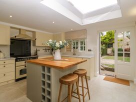 A kitchen with an island, stools, and a door opening to the garden at The Cottage in Stow-On-The-Wold