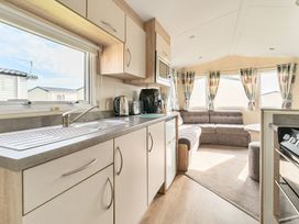 A kitchen area with cupboards sink kettle toaster and microwave leading to a living area with sofa windows and curtains at Golden Dune - Hayling Island in Hayling Island Holiday Park