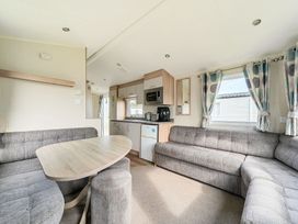 A living area with grey upholstered seating a wooden dining table a kitchen area with cabinets microwave and appliances at Golden Dune - Hayling Island in Hayling Island Holiday Park