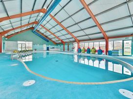 An indoor swimming pool with a pool ladder and colorful seating at Golden Dune - Hayling Island