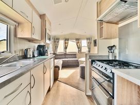 A kitchen with appliances and cabinets leading to a living area with a sofa and windows at Anchor's Rest - Hayling Island Hayling Island Holiday Park