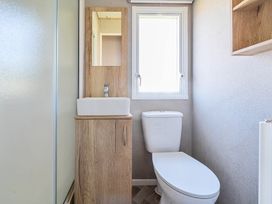 A bathroom with a toilet a sink with cabinet a mirror and a window at Dune Delight - Hayling Island Hayling Island Holiday Park