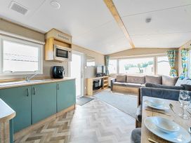 An open-plan living room and kitchen with blue cabinets a grey sofa a dining table set with plates and glasses and large windows at Dune Delight - Hayling Island in Hayling Island Holiday Park