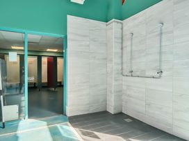 A shower area with two showerheads and a tiled floor next to a changing room with benches and cubicles at Beachcomber's Base - Hayling Island in Hayling Island Holiday Park
