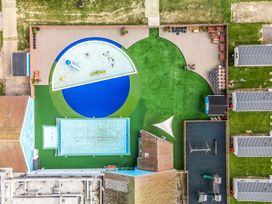An aerial view of a playground with a splash pad small pool swings slide and green grassy areas at Beachcomber's Base - Hayling Island in Hayling Island Holiday Park
