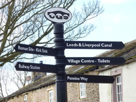 A black directional signpost with multiple signs pointing to local sites including Leeds Liverpool Canal Roman Site Kirk Sink Railway Station Village Centre Toilets and Pennine Way