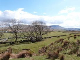 A rural landscape with grassy fields, leafless trees, stone walls, and hills in the background at Kingfisher Lodge in Gargrave