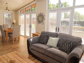 A living room with a gray sofa and dining table with chairs near large windows at Kingfisher Lodge in Gargrave