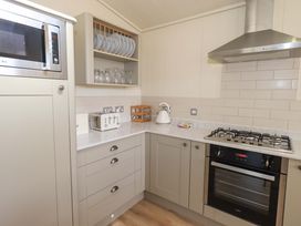 A kitchen corner with a microwave oven plates glasses a toaster a kettle and a gas stove with an oven at Kingfisher Lodge in Gargrave