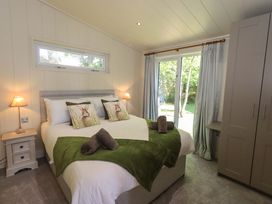 A bedroom with a double bed with green throws and rabbit cushions two lamps a wardrobe and sliding glass doors to the garden at Kingfisher Lodge in Gargrave
