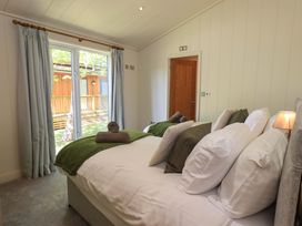 A bedroom with two beds, pillows, rolled towels, a lamp, curtains over a glass door, and a wooden door at Kingfisher Lodge in Gargrave