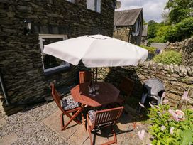 An outdoor area with a wooden table and chairs under an umbrella at Poppy Cottage in Bowness-On-Windermere
