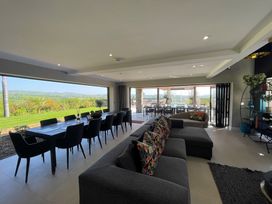 A living room with a long dining table and chairs next to large open windows showing a garden at Forest Lodge in Pontyclun