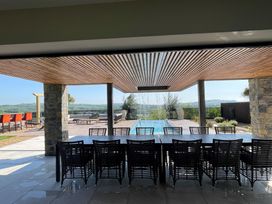 An outdoor dining area with a long table and chairs under a wooden ceiling near a pool at Forest Lodge in Pontyclun