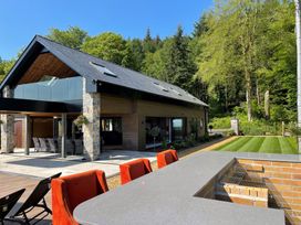 Outdoor patio area with orange chairs and barbecue near a modern house with glass balcony and lawn at Forest Lodge in Pontyclun