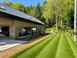 A modern house with a glass dining room opening to a striped lawn and trees at Forest Lodge in Pontyclun