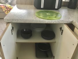 A kitchen countertop with a cutting board and plates in a cabinet at 38 The Green