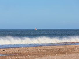 A beach with waves and a sailing boat on the ocean at Rigg Cottage, Mount Pleasant Sandsend