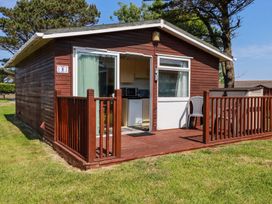 A small wooden cabin with a sliding glass door and a small porch with plastic chairs at 101 Atlantic Bays Holiday Park in Padstow