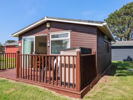 A small wooden cabin with a deck and railing outside on grass at 101 Atlantic Bays Holiday Park in Padstow