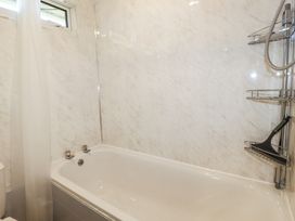 A bathroom with a white bathtub shower curtain and a metal shower caddy with a squeegee at 101 Atlantic Bays Holiday Park Padstow