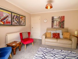 A living room with a beige sofa and patterned cushions a red chair a blue chair wooden side tables wall art a clock and a light fixture at 3 Birkbeck Way in Norwich