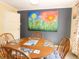 A dining room with a round wooden table and chairs and a colorful flower painting on a gray wall at 3 Birkbeck Way in Norwich