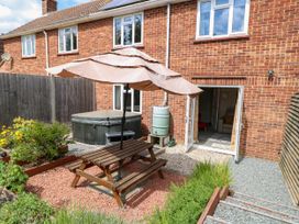 A backyard with a wooden picnic table and umbrella a hot tub plants and open doors leading inside at 3 Birkbeck Way Norwich