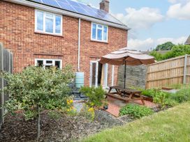 A backyard garden with a wooden picnic table and umbrella beside a brick house with solar panels at 3 Birkbeck Way in Norwich