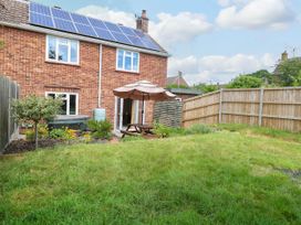 A backyard with a wooden picnic table under an umbrella solar panels on a brick house roof and a grass lawn at 3 Birkbeck Way in Norwich