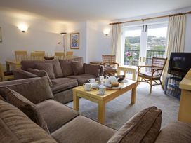 A living room with brown sofas a wooden coffee table set with cups and plates two chairs by a window with curtains and a dining table with chairs at 10 Dartmouth House in Dartmouth