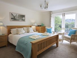A bedroom with a wooden bed blue bedding two wicker chairs with blue cushions and glass doors at 10 Dartmouth House in Dartmouth