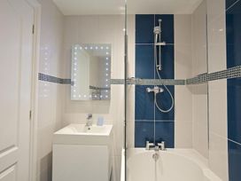 A bathroom with a white sink, a mirror with lights, a bathtub, and a shower with blue and white tiles at 10 Dartmouth House in Dartmouth