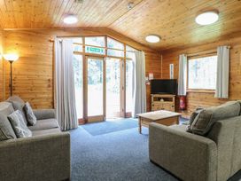 A living room with two gray sofas a wooden coffee table a standing lamp a TV on a wooden stand and large windows at Sycamore Lodge in Rosliston