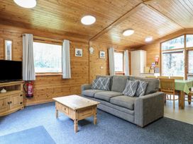 A wooden living room with a gray sofa and a wooden coffee table with a dining area in the background at Sycamore Lodge in Rosliston