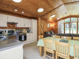 A kitchen and dining area with wooden chairs a green tablecloth and gray sofas at Sycamore Lodge in Rosliston